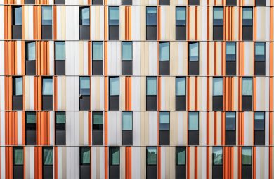 zdjęcie eelewacji nowoczesnego budynku z czarnymi oknami i pomarańczowo biało beżową elewacją