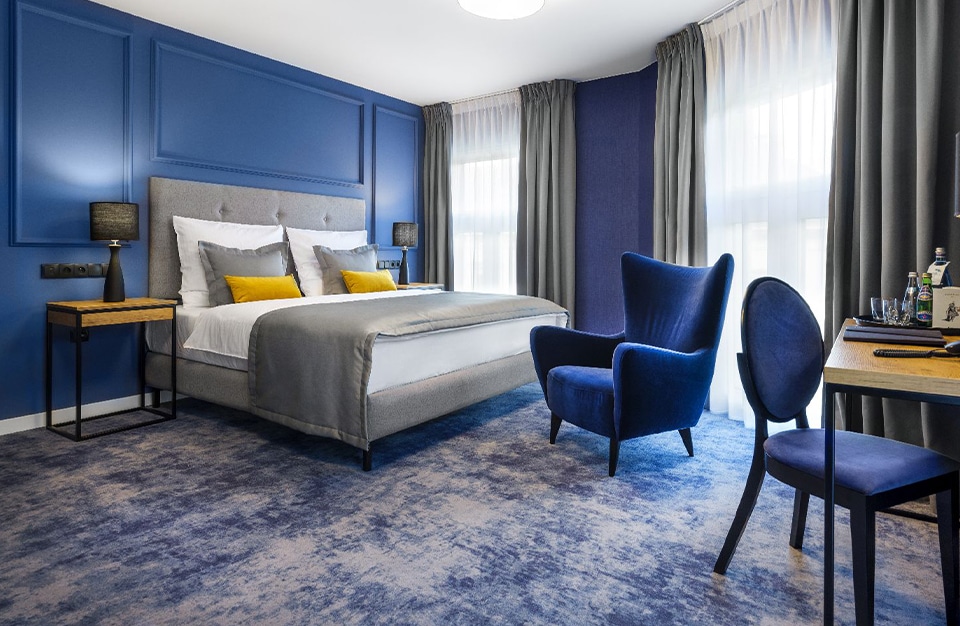 ibis Styles Santorini niebieski fotel w pokoju hotelowych z dużym łóżkiem z żółtymi poduszkami