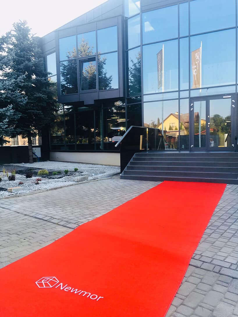 czerwony dywan z napisem Newmor rozwinięty przed wejściem do biurowca