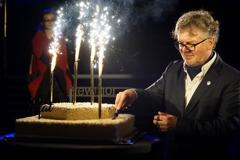 mężczyzna w okularach kroi tort z wpitymi sztucznymi ogniami