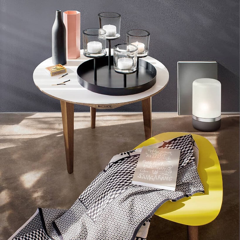 żółty stołek z materiałem w szare kropki przy białym stoliku z czarnym świecznikiem