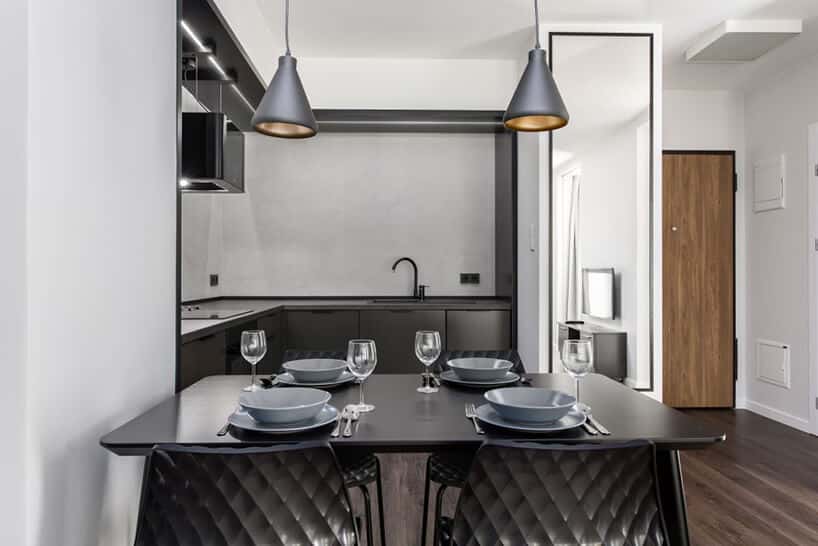 czarny stół z zastawą na tle ciemno szarego aneksu kuchennego we wnętrzu apartamentu w gdańskim Dekorian Home projektu Studio Poziom