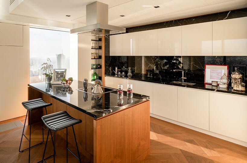 mała drewniana wyspa kuchenna z czarnym kamiennym nowoczesny apartament projektu Anny Koszeli na tle kuchni z białym frontami szafek i czarnym kamiennym blatem wraz z czarną kamienną ścianą