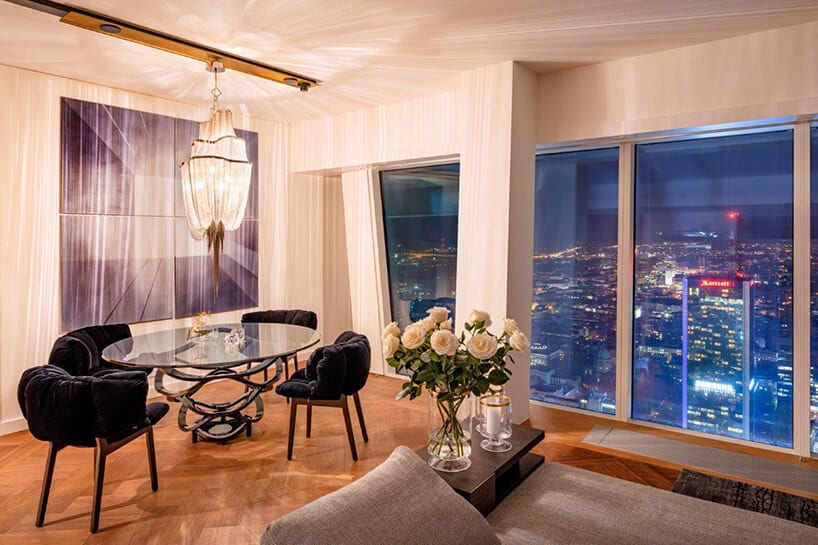nowoczesnych stół ze szklanym blatem w nowoczesnym apartament projektu Anny Koszeli pod wyjątkowym żyrandolem na tle obrazu obok widoku na rozświetloną nocną Warszawę