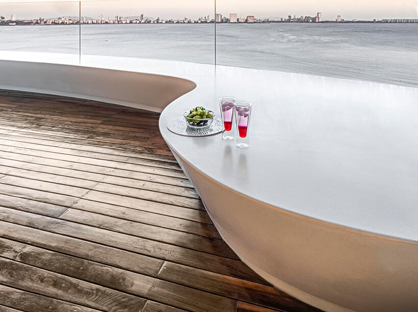 ekskluzywny apartament projektu ZZ Architects drewniany taras z długim białym siedziskiem na tle rzeki z zarysem miasta
