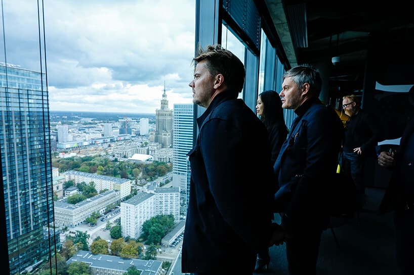 kilka osób przy oknach budynku na wysokim piętrze na tle panoramy Warszawy