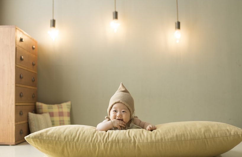 dziecko na jasnej poduszce na tle ściany i wiszących u góry lamp