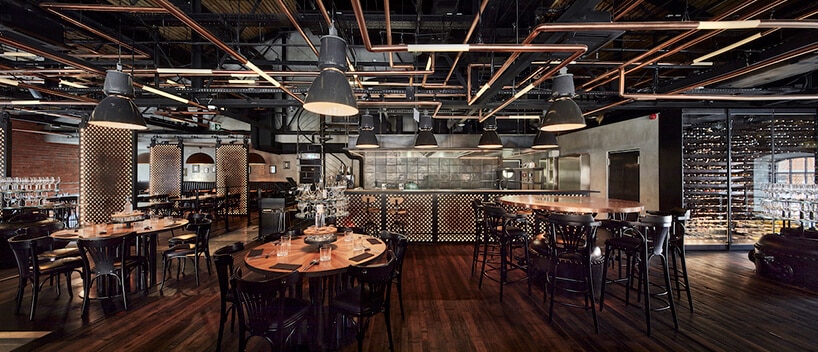 industrialne wnętrze restauracji Zoni eleganckie drewniane stoliki z czarnymi krzesłami na tle kuchni