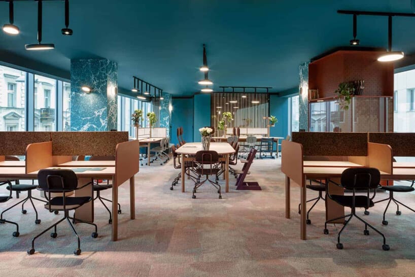 niebieskie wnętrze The Nest od Beza Projekt przestrzeni biurowej z drewnianymi biurkami stołami i krzesłami w open space