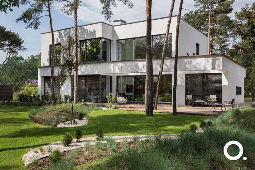 biały dom piętrowy z z ogrodem zgodnego z biophilic design od Studio.O. na tle drzew iglastych