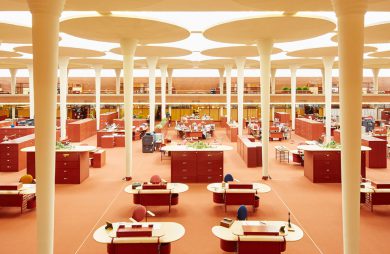 pomarańczowe wnętrze biurowca Johnson Wax Headqarters z owalnymi biurkami sufitem przepuszczającym światło przez zamglone panele z wysokimi filarami