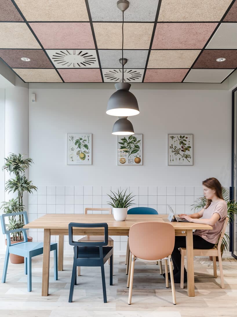 ekologiczne biuro od workplace solutions biała przestrzeń z dużym drewnianym stole z kolorowymi krzesłami na tle białej ściany z plakatami owoców
