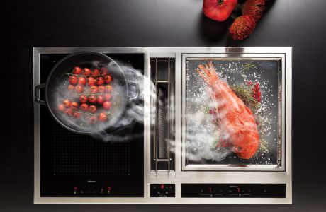 czarna ze srebrną ramką płyta indukcyjna ze zintegrowanym okapem podczas gotowania czerwonej ryby i pomidorów
