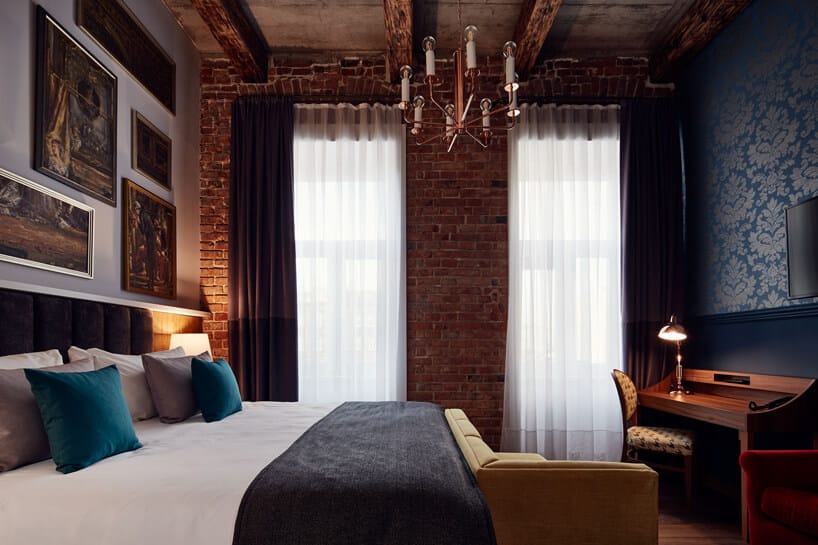 pokój hotelowy z dużymi łóżkiem i biurkiem na tle ściany z cegieł i drewnianego sufitu
