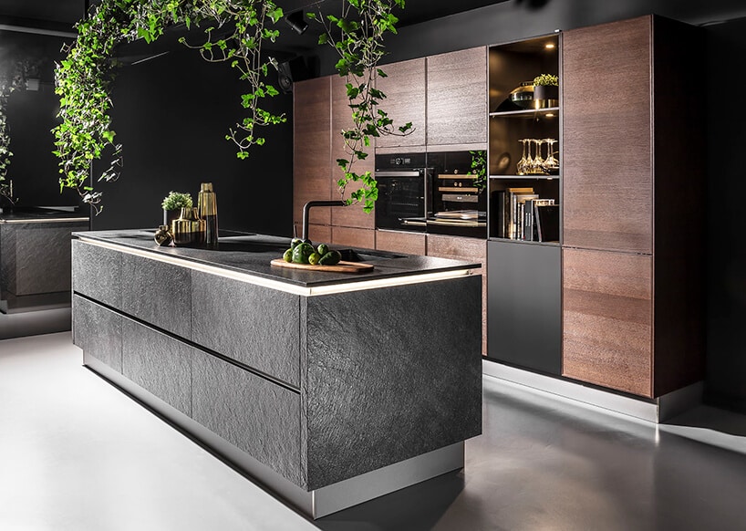 elegancka kuchnia z brązową zabudową i dużą wyspą wykończoną czarnym kamieniem z czarnym blatem