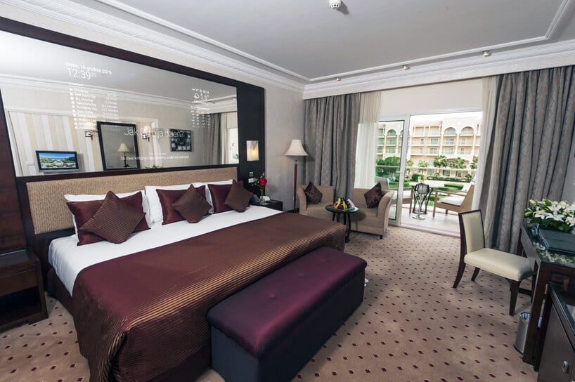 duże interaktywne inteligentne lustro od Mirror Investment w eleganckim pokoju hotelowym nad dużym łóżkiem