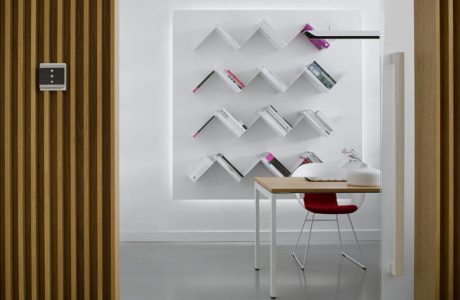 nowoczesne białe wnętrze małe biurko z czerwony krzesłem na tle ściany z trójkątnymi półkami na książki z panelem sterującym ABB na drewnianej ścianie