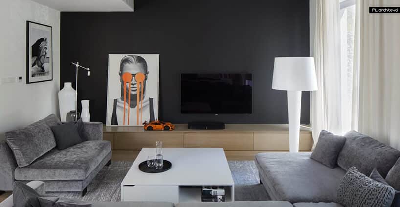 elegancki salon z szarumi sofami długą szafką drewnianą na tle czarnej ściany z telewizorem