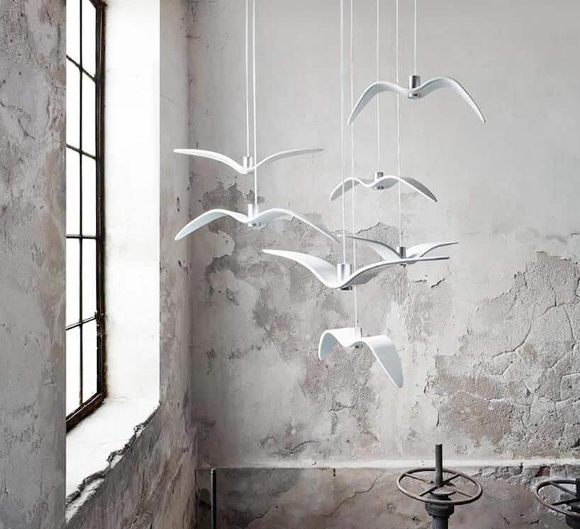 białe wiszące lampy Night Birds od Brokis wygięty metal w kształcie lecących ptaków na tle betonowej ściany