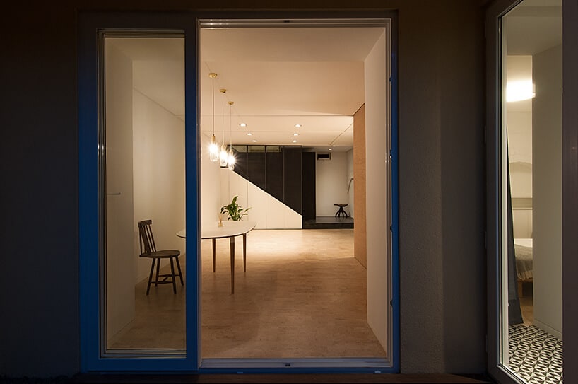 loft projektu KEMA studio jasny salon z drewnianym stołem widziany nocą przez otwarte drzwi