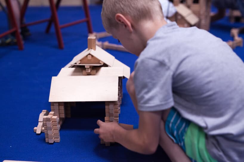 chłopiec budujący dom z drewnianych klocków na niebieskiej wykładzinie