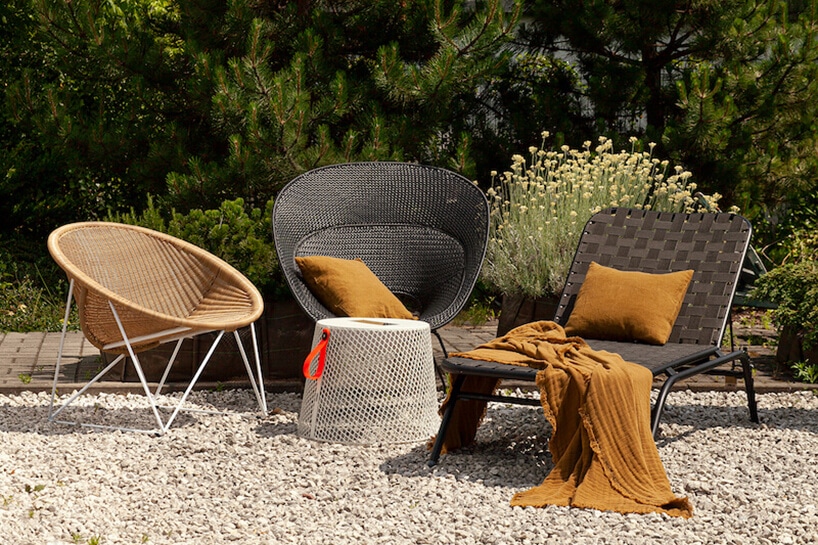 trzy rożne eleganckie krzesła zewnętrzne Bertoia Side Chair od Knoll na kamienistym tarasie na tle iglastych drzew
