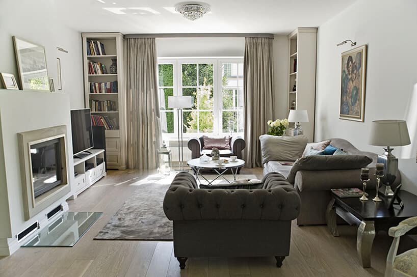 eleganckie wnętrze projektu Miśkiewicz Design jasny salon z zabudowanym kominkiem na tle wysokiego białego okna
