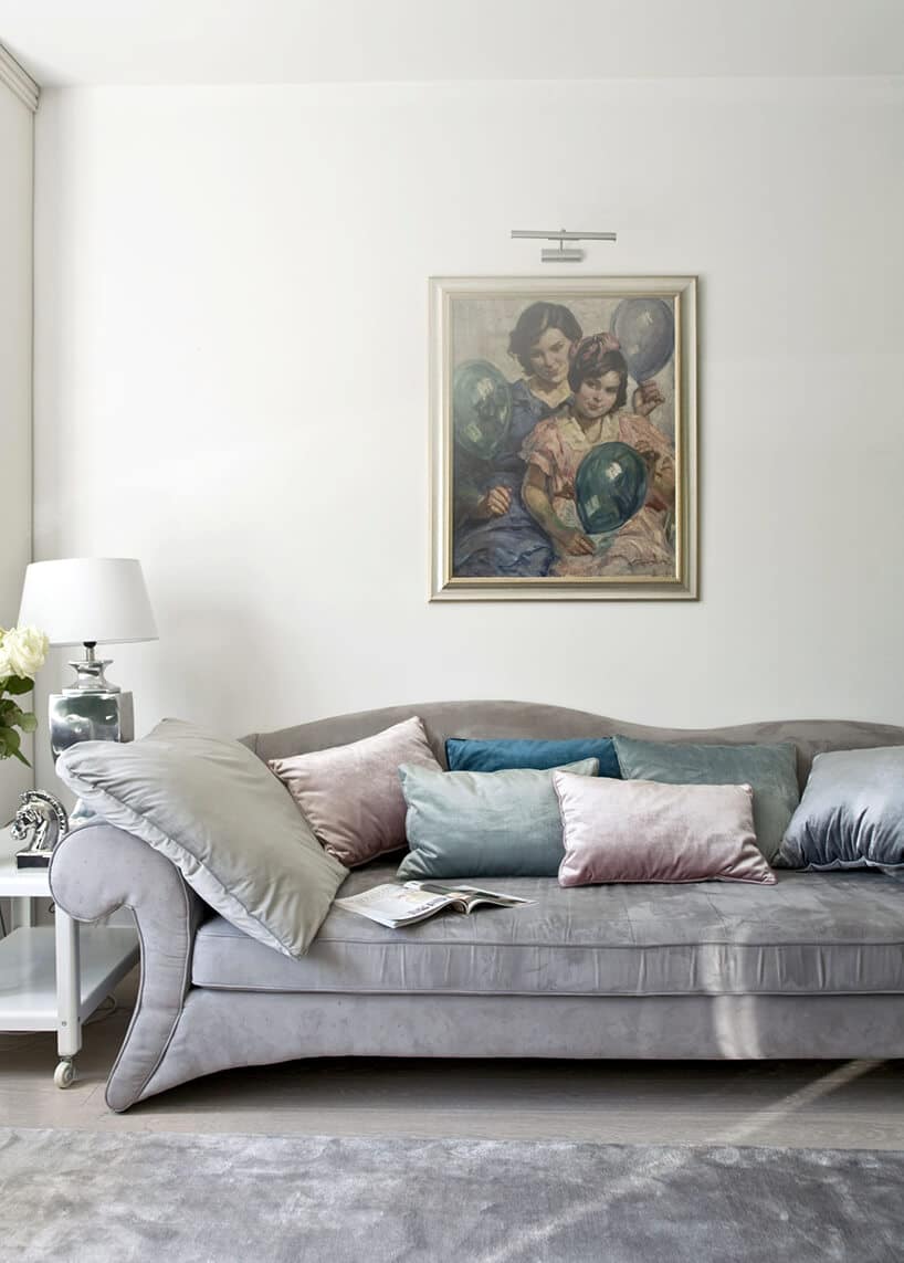 eleganckie wnętrze projektu Miśkiewicz Design elegancka srebrna sofa z błyszczącymi poduszkami dekoracyjnymi pod obrazem na jasnej ścianie