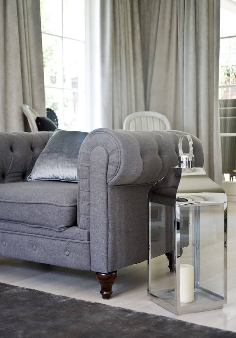 eleganckie wnętrze projektu Miśkiewicz Design szary fotel z niskim oparciem obok zabudowanego świecznika w kształcie lampionu