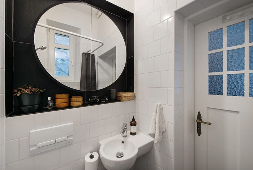biała łazienka z okrągłym lustrem w czarnej wnęce