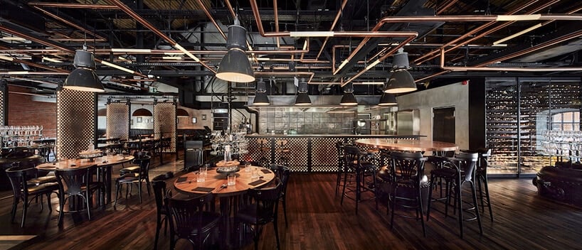 industrialne wnętrze restauracji Zoni projektu Mirosława Nizio przestrzeń restauracyjna z drewnianymi stolikami z czarnymi krzesłami pod przemysłowymi dużymi lampami