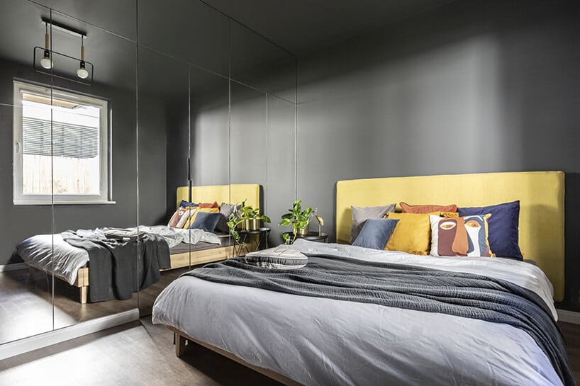 sypialnia w ciemnej kolorystyce z dużym lustrem oraz cytrynowo żółtym zagłówkiem i jasno szarymi akcesoriami