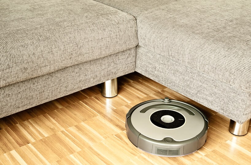 automatyczny okrągły robot sprzątający na drewnianej podłodze przy szarej sofie