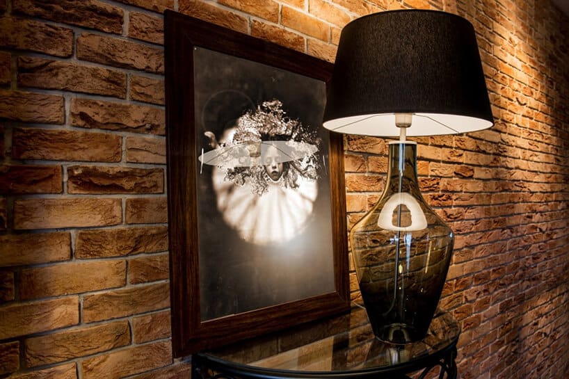 elegancka ciemna lampa Kallisto od Dekoluce ze szklaną przeźroczystą podstawową z ciemnym kloszem na szklanym stoliku na tle ceglanej ściany