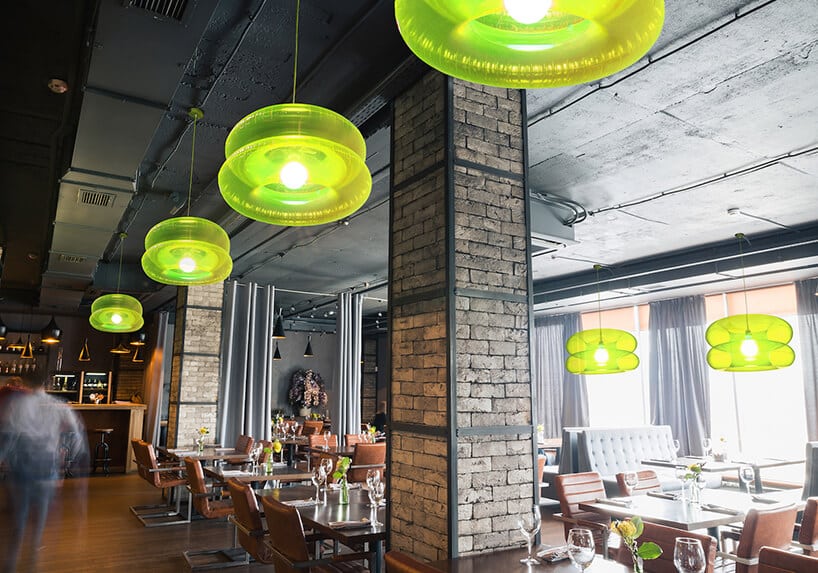 zielone lampy Big Lime od Puff-Buff w restauracji z czarnym betonowym sufitem i ceglanymi filarami