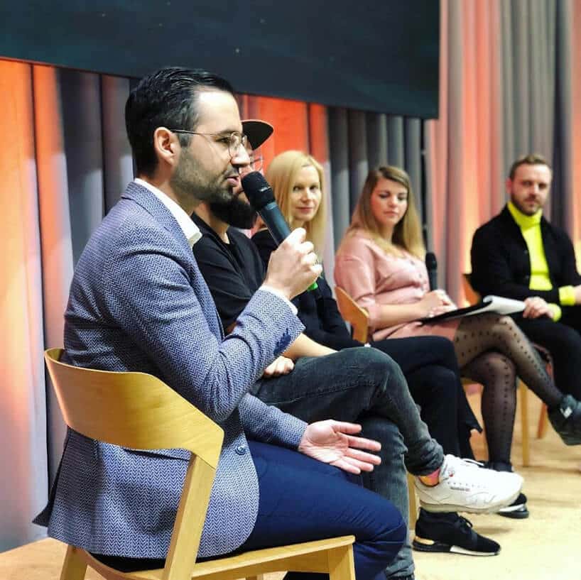 mężczyzna w niebieskiej marynarce podczas rozmowy na słuchacze podczas panelu MAGAZIF na Arena Design 2019