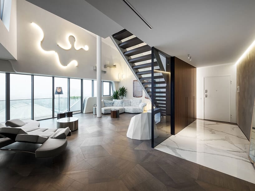 elegancki penthouse od Zaha Hadid elegancki wysoki salon z ciemną drewniana podłoga i ciemnymi schodami na górę