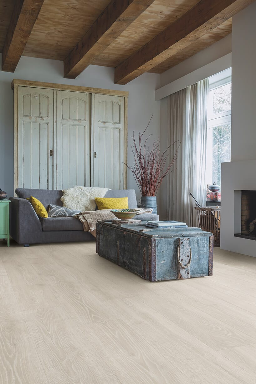 jasne podłoga laminowana Quick-Step w salonie w ze starą niebieska skrzynią przerobioną na stolik obok komina