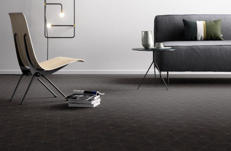ciemna podłoga winylowa w geometryczne kształty pod szarą sofą i metalowo-drewnianym nowoczesnym krzesłem