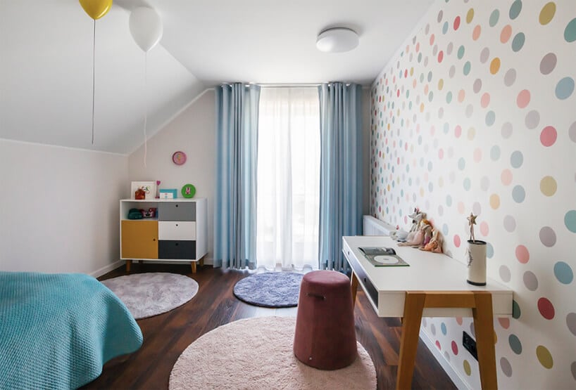 biały pokój dla dziewczynki na poddaszu z ciemną drewniana podłogą i tapetą w kolorowe kółka