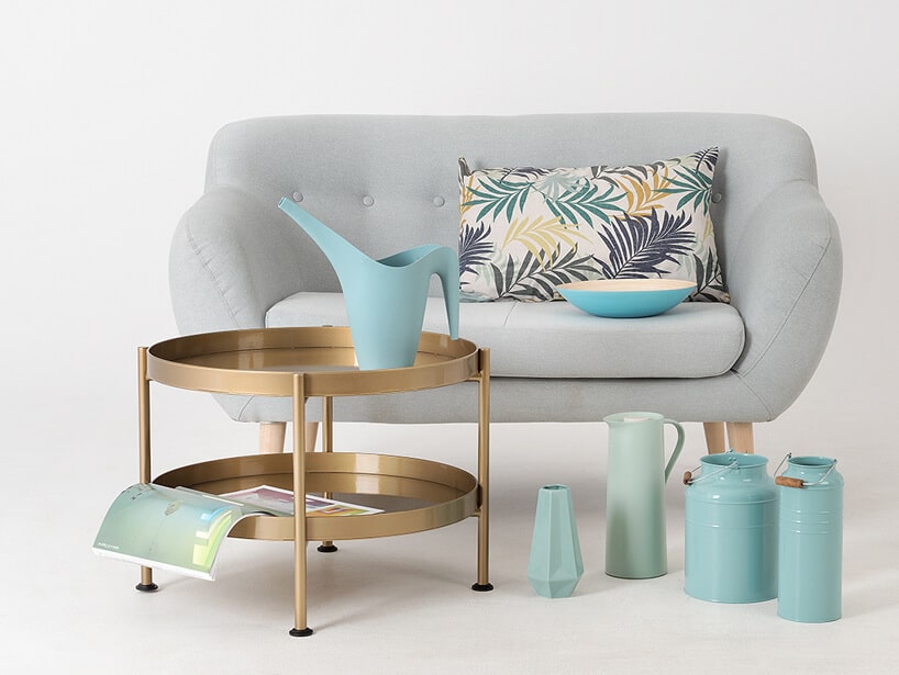 mała szara sofa jako tło dla różnych naczyń metalowych i porcelanowych obok okrągłego dwupoziomowego stolika