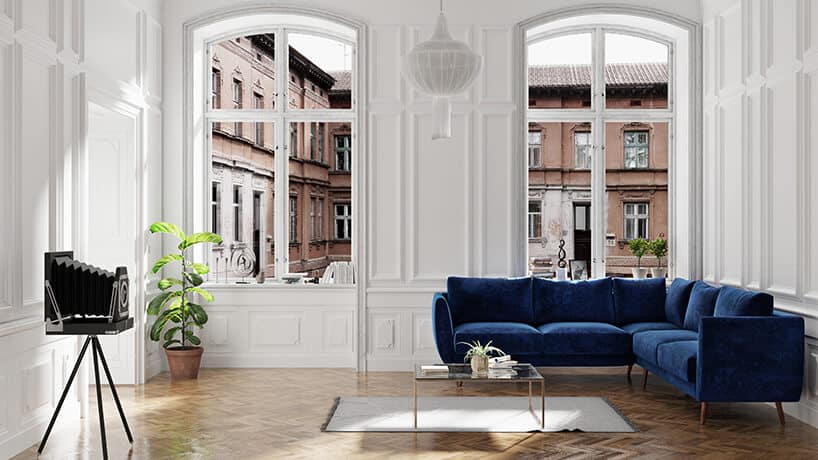 elegancka ciemno niebieska sofa narożna od Scandisofa na tle starego okna z widokiem na kamienice