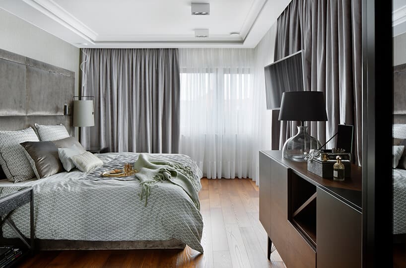 elegancki apartament Hola Design z nagrodą EPA 2019-2020 przestronna sypialnia z brązową drewnianą podłogą z dużym szarym łóżkiem o ciemną brązową szafką