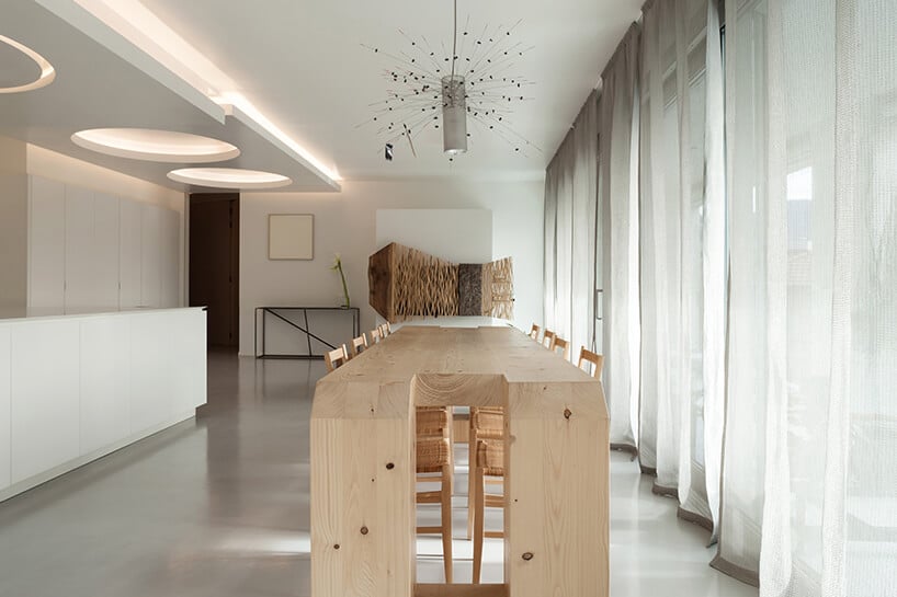 salon z białą aranżacją oraz długimi zasłonami oraz nietypowym wysokim drewnianym stołem