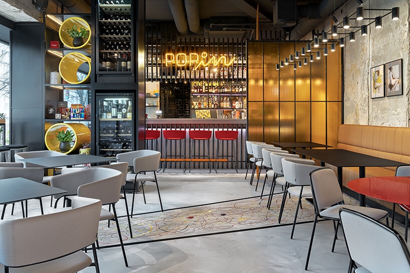 wnętrze restauracji POP in projektu Sikora Wnętrza czarne stoliki z szarymi krzesłami na tle baru z neonem POPin