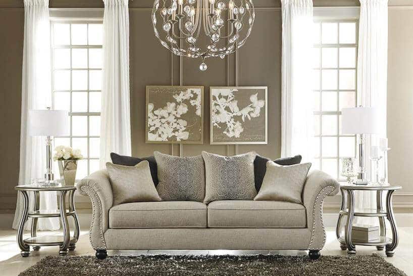 jasne eleganckie wnętrze w stylu angielskim beżowa sofa pomiędzy dwoma metalowymi stolikami pod żyrandolem ze szklanymi ozdobami