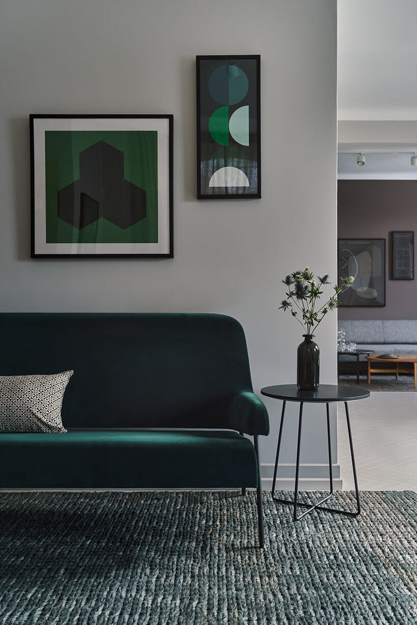 ciemno zielona sofa obok małego okrągłego stolika na dywanie z dużych nici