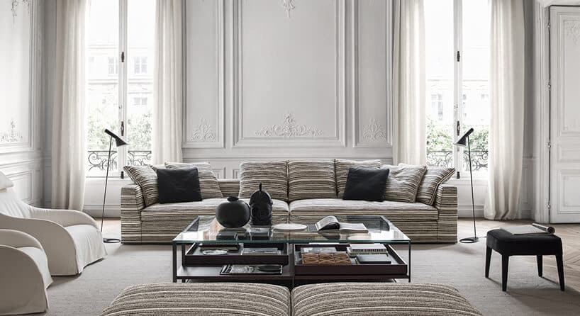 długa sofa Otium Soft Maxalto w kolorowe kreski z poduszkami na tle zdobionej ściany z wysokimi oknami
