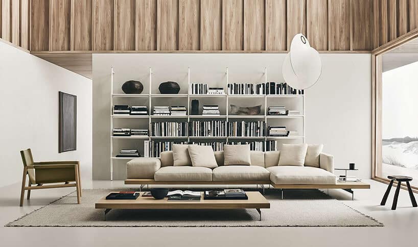 nowoczesna beżowa sofa Dock od B&B Italia na dużej drewnianej ramie z cienkimi metalowymi nogami na tle białej szafki z metalowych prętów
