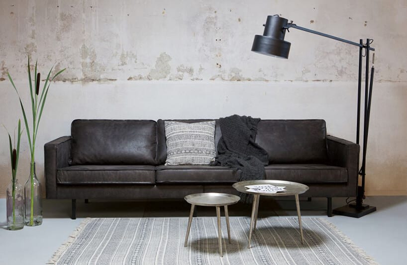 czarna skórzana sofa Rodeo od BE Pure obok duże czarnej lampy na ramieniu na tle szarej ściany